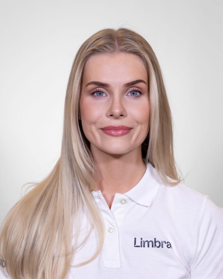 Kvinne med lang blond hår i hvit Limba-trøye smilende mot kamera.
