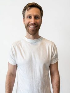Mann med hvit t-skjorte smilende mot hvit bakgrunn.