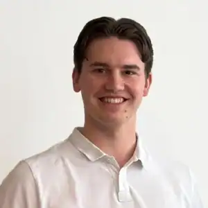 Ung mann med mørkt hår og hvit skjorte smiler mot kamera.