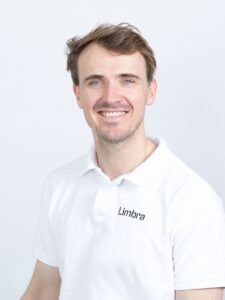 Kiropraktor Tomas Mills smiler i hvit Limbraklær mot hvit bakgrunn.