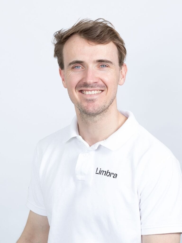 Kiropraktor Tomas Mills smiler i hvit Limbraklær mot hvit bakgrunn.