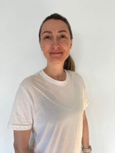 Kvinne med lyst hår og hvit t-skjorte smilende mot kamera.