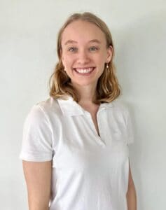 Smilende kvinne i hvit polo, portrett mot lys bakgrunn.