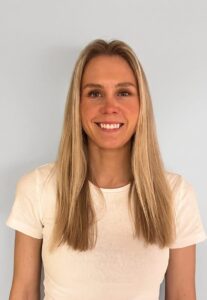 Smilende kvinne med langt blondt hår i hvit t-skjorte foran lys bakgrunn.