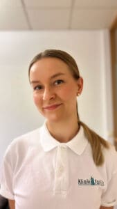 Kvinne i hvit polo med Limbra-logo, smilende, innendørs.