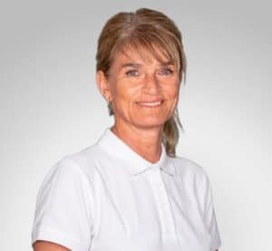 Kvinne i hvit polo smilende mot kamera, helsepersonell.