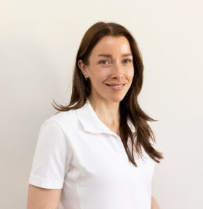 Kvinne i hvit polo smiler mot kamera, portrettfoto.