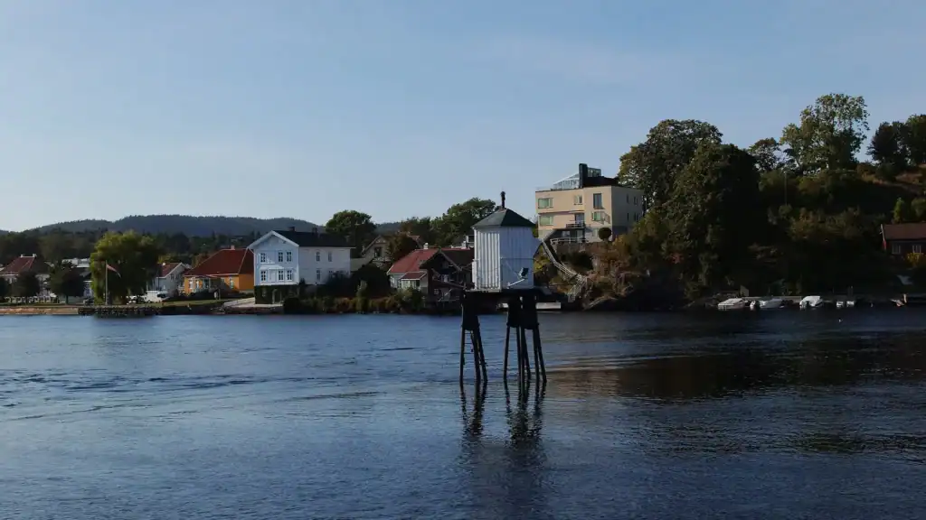 Havnby med hus langs vannkanten og en brygge i forgrunnen.