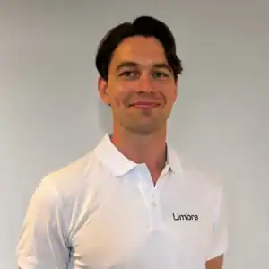 Kiropraktor i hvit t-skjorte med Limbra-logo smiler til kamera.