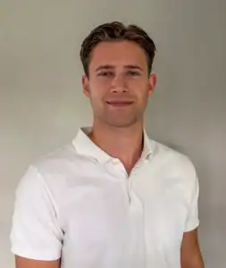 Ung mann i hvit polo shirt smiler mot kamera.