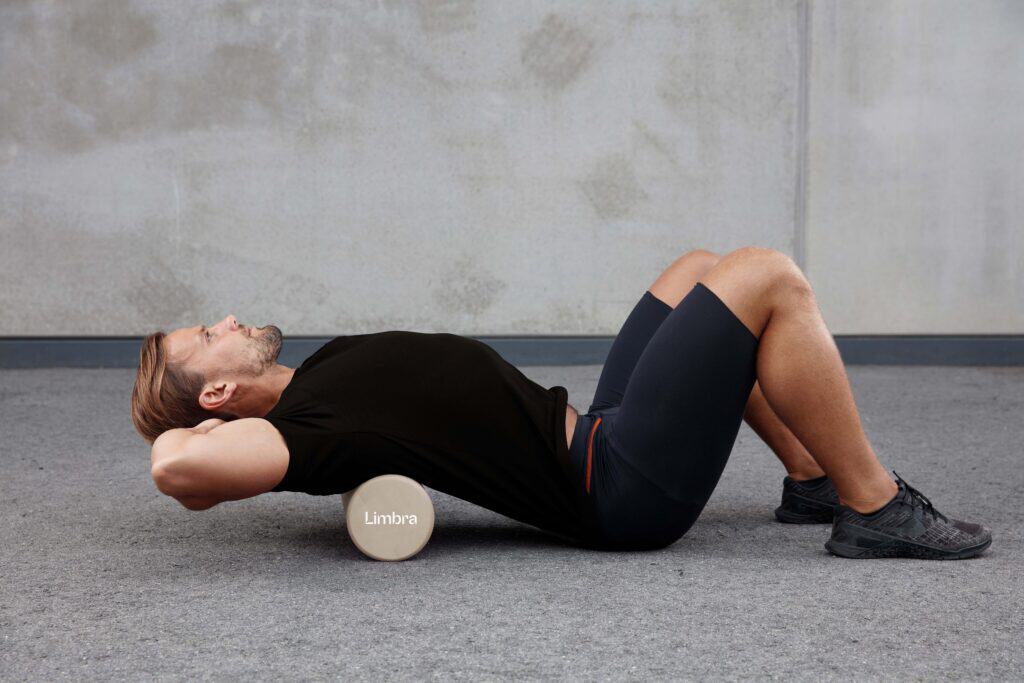 Man gör ryggövning med foam roller bakom huvudet.