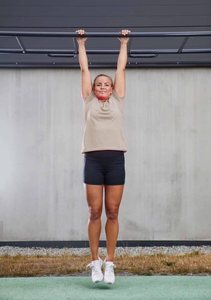 Kvinna gör pull-up utomhus under tak.
